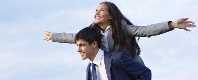 a male business professional with a female business professional on his back, piggy-back style.