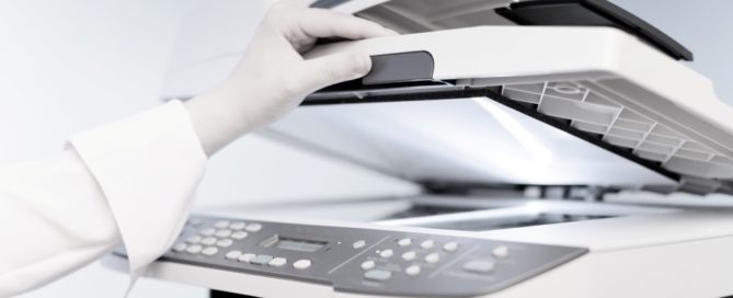 A professional woman's hand lifting up the top of a copier to scan a document